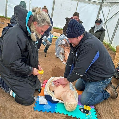 Learners practising CPR and defibrillator use on a manikin during a training course